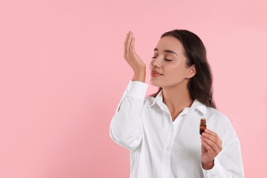 Photo of Beautiful young woman with bottle of essential oil on pink background, space for text