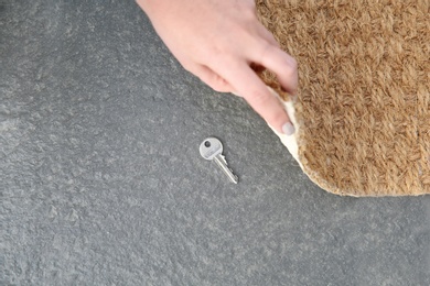 Photo of Young woman revealing hidden key under door mat, top view with space for text