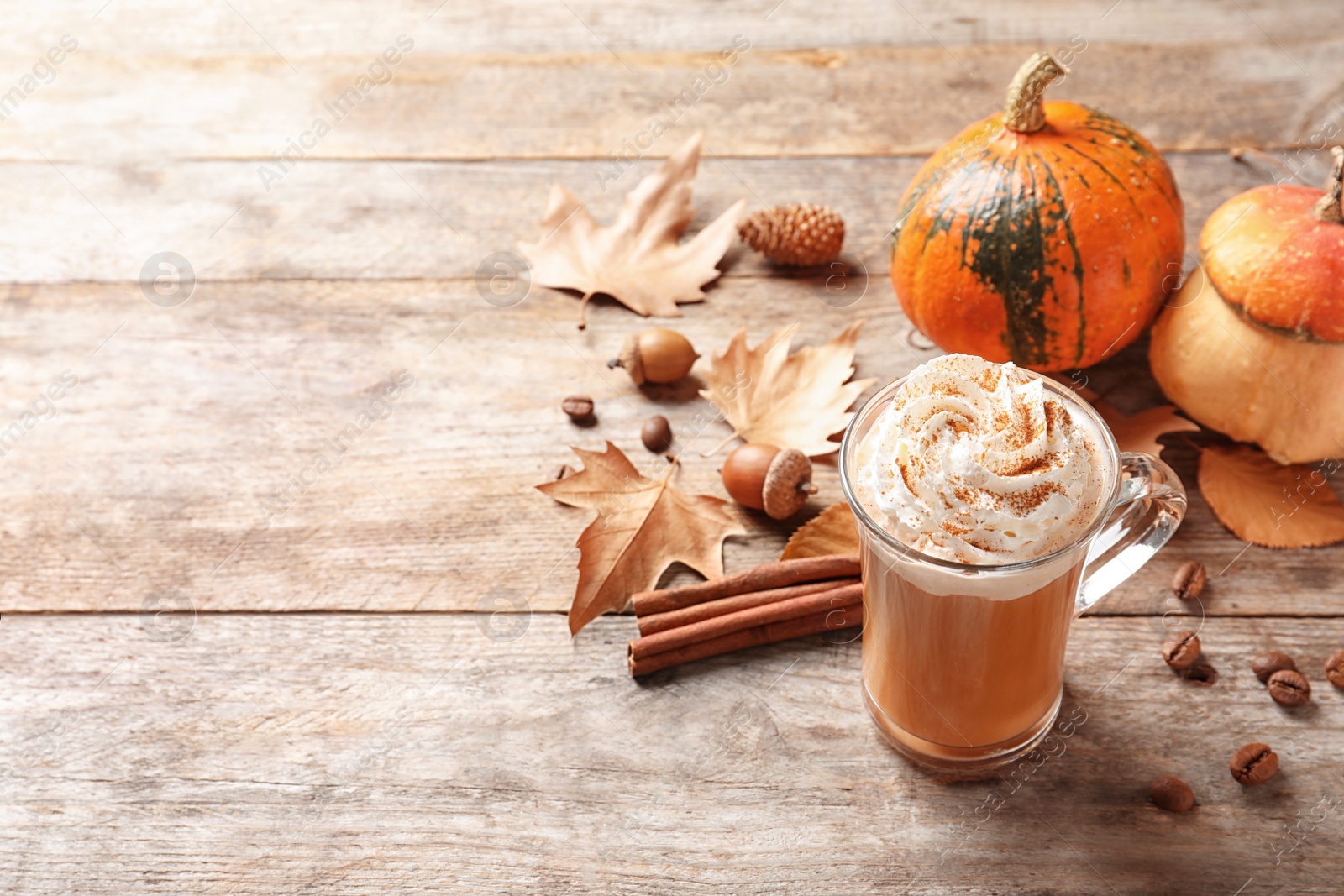 Photo of Glass cup with tasty pumpkin spice latte and space for text on wooden table