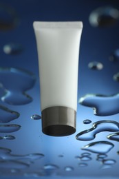 Moisturizing cream in tube on glass with water drops against blue background, low angle view
