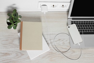 Photo of Laptop and smartphone charging on wooden table, above view