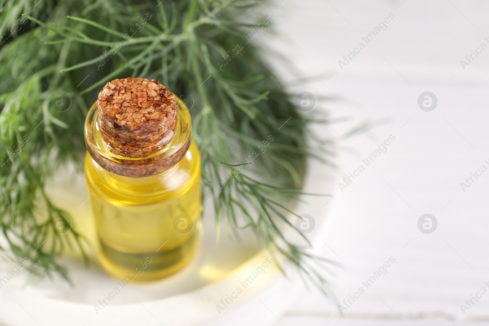 Photo of Bottle of essential oil and fresh dill on white table, closeup. Space for text