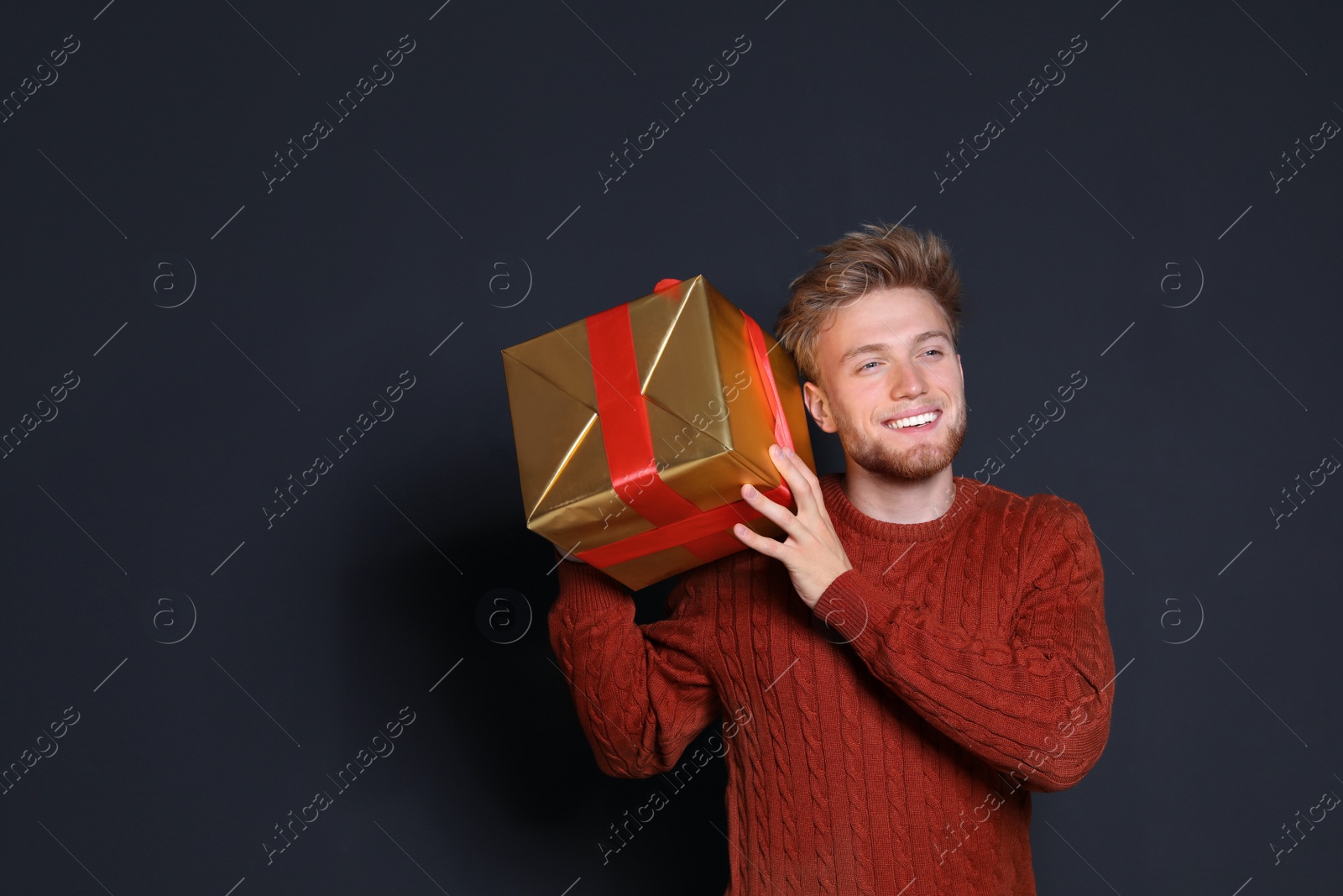 Photo of Young man with Christmas gift on dark background. Space for text