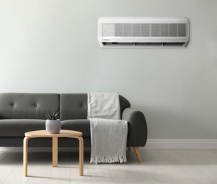 Image of Modern air conditioner on white wall in room with stylish grey sofa