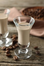 Photo of Coffee cream liqueur in glasses and beans on wooden table, closeup