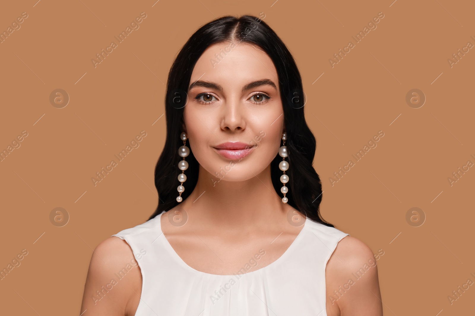 Photo of Young woman wearing elegant pearl earrings on brown background