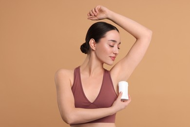 Photo of Beautiful woman applying deodorant on beige background