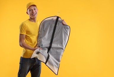 Dry-cleaning delivery. Happy courier holding garment cover with clothes on orange background, space for text