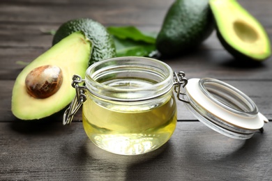 Jar of natural oil and avocados on wooden background