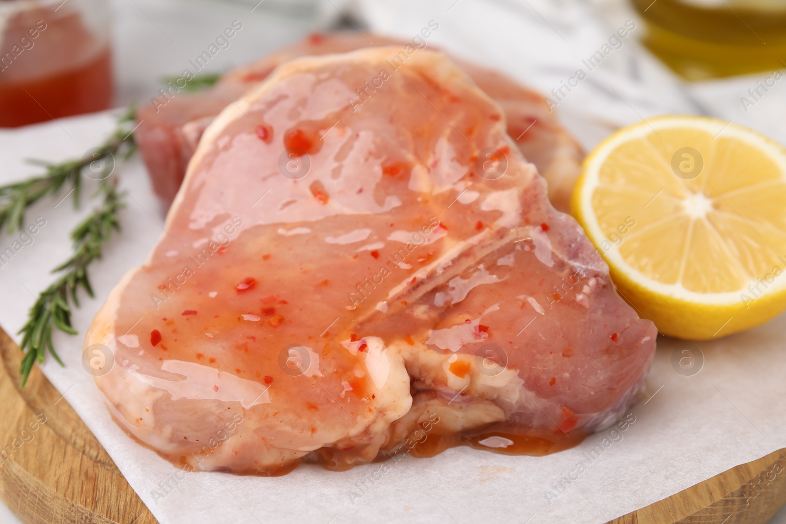 Photo of Board with raw marinated meat, lemon and rosemary on table, closeup