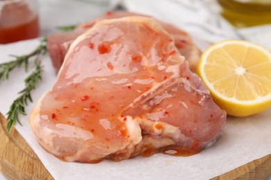 Photo of Board with raw marinated meat, lemon and rosemary on table, closeup