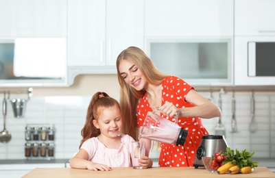 Photo of Young woman pouring delicious milk shake into glass for her daughter in kitchen
