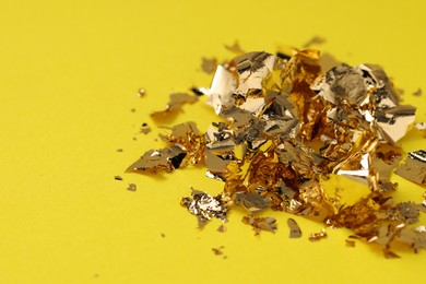 Photo of Many pieces of edible gold leaf on yellow background, closeup