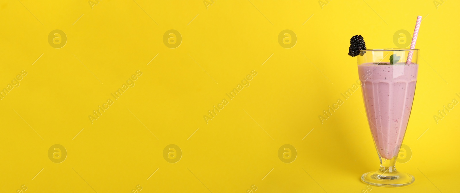 Photo of Tasty fresh milk shake with blackberry on yellow background. Space for text