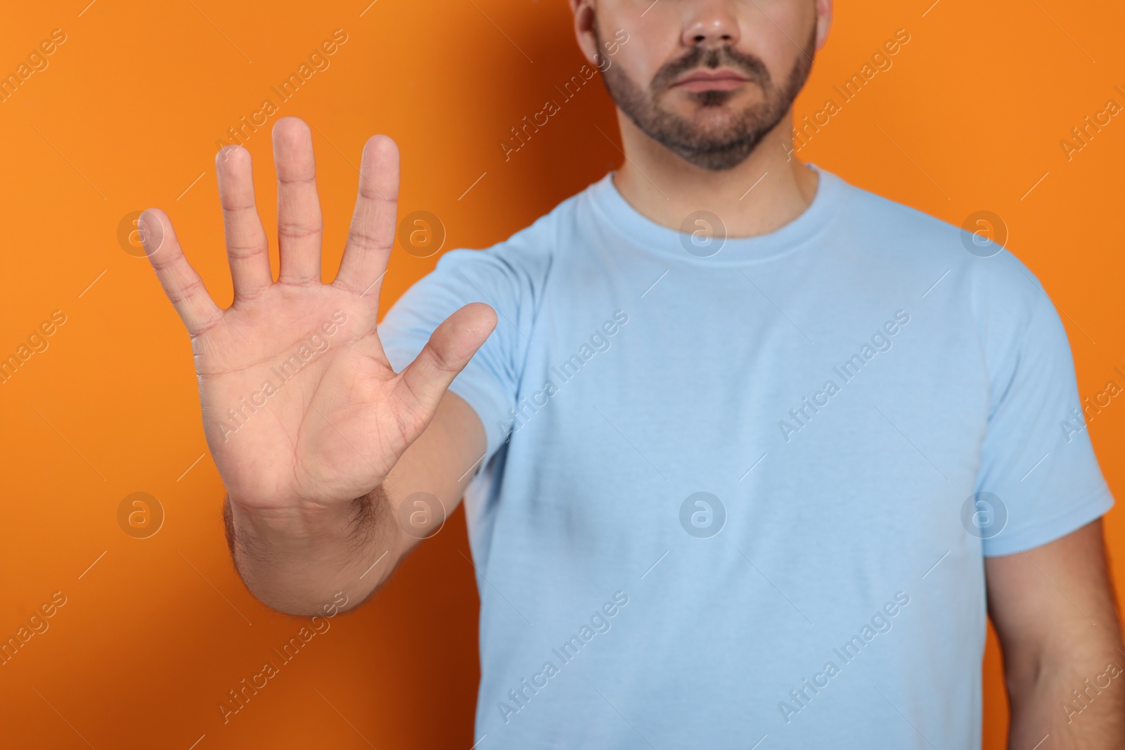 Photo of Man showing stop gesture on orange background, closeup