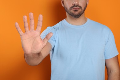 Man showing stop gesture on orange background, closeup