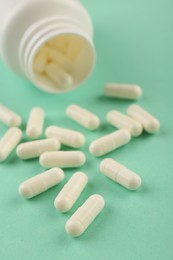 Bottle and vitamin capsules on turquoise background, closeup