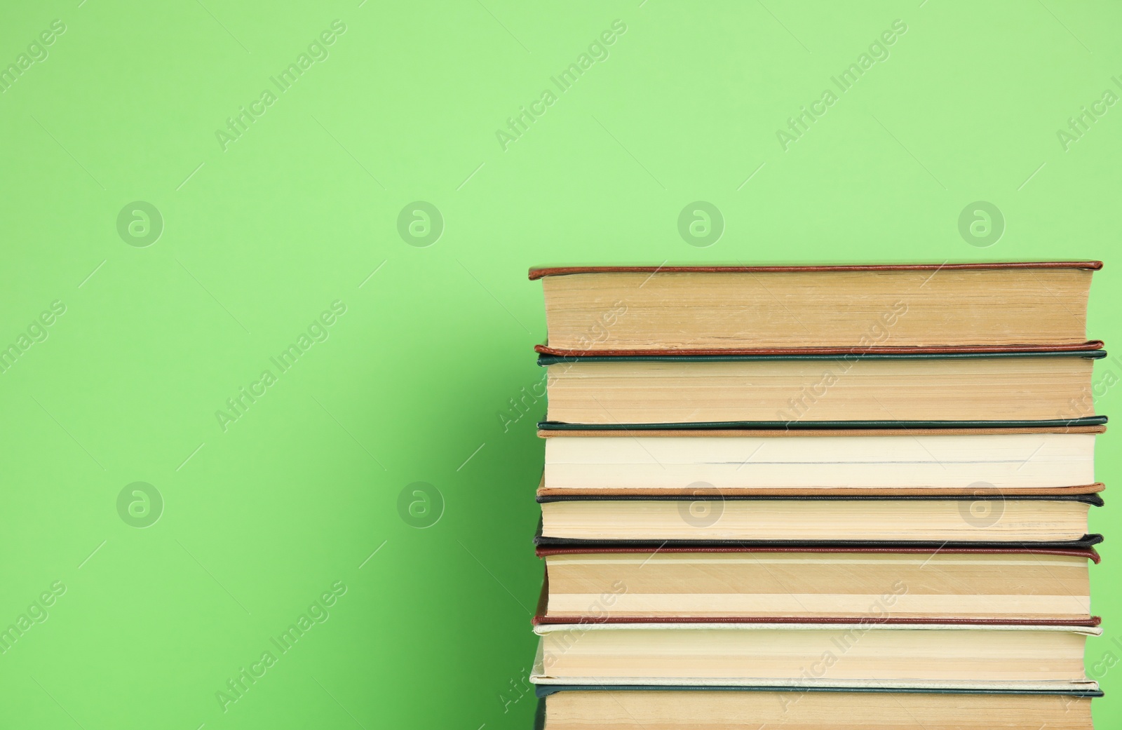 Photo of Stack of hardcover books on green background. Space for text