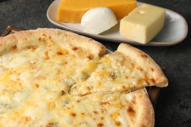 Photo of Delicious cheese pizza and different kinds of cheese on dark grey table, closeup