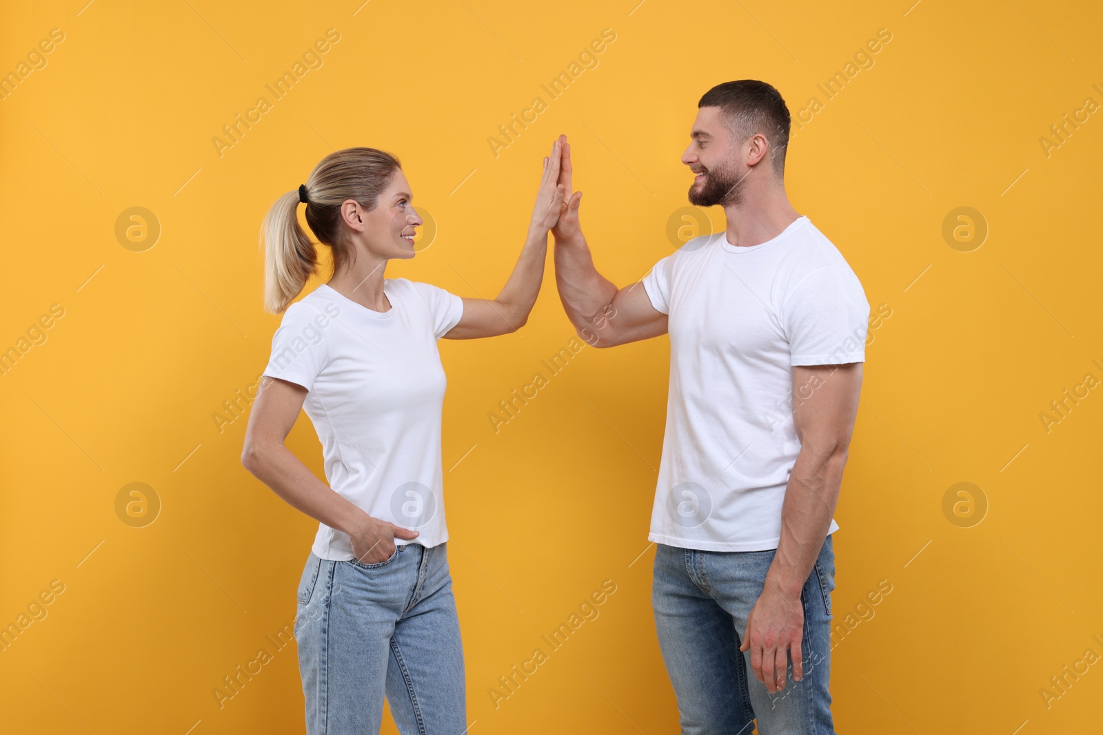 Photo of Happy couple giving high five on orange background