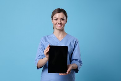 Doctor holding blank tablet on light blue background, space for design