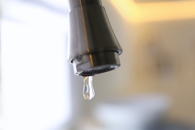 Photo of Water drop falling down from tap on blurred background, closeup