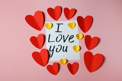 Photo of Frame made of paper hearts and card with phrase I LOVE YOU on pink background, flat lay