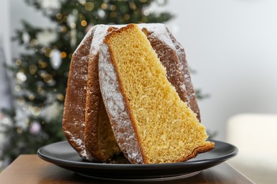 Delicious Pandoro cake decorated with powdered sugar near Christmas tree in room. Traditional Italian pastry