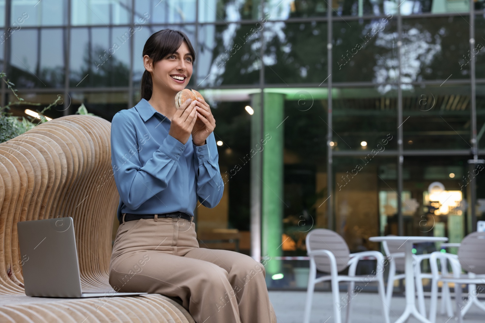 Photo of Lunch time. Happy businesswoman with hamburger on bench outdoors