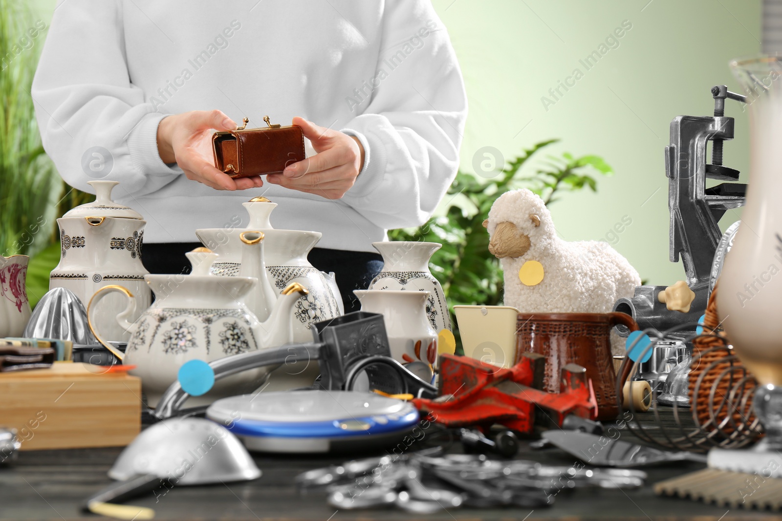 Photo of Woman holding vintage wallet above table with different stuff indoors, closeup. Garage sale