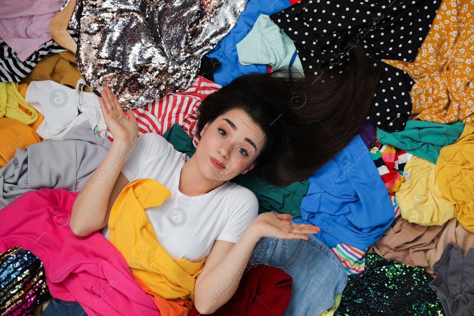 Photo of Young woman with lots of clothes on floor in room, top view. Fast fashion