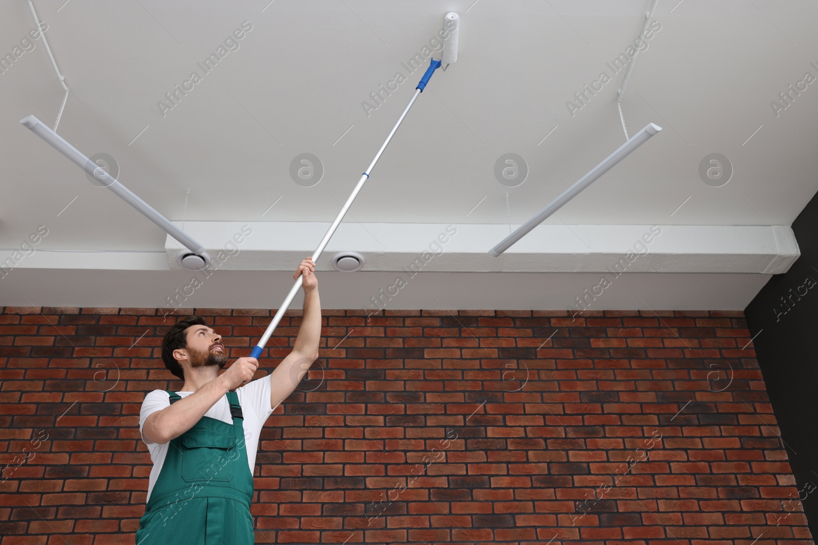 Photo of Handyman painting ceiling with roller in room, low angle view