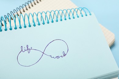 Photo of Drawn infinity sign with words Work and Life in notebook on light blue background, closeup. Balance concept