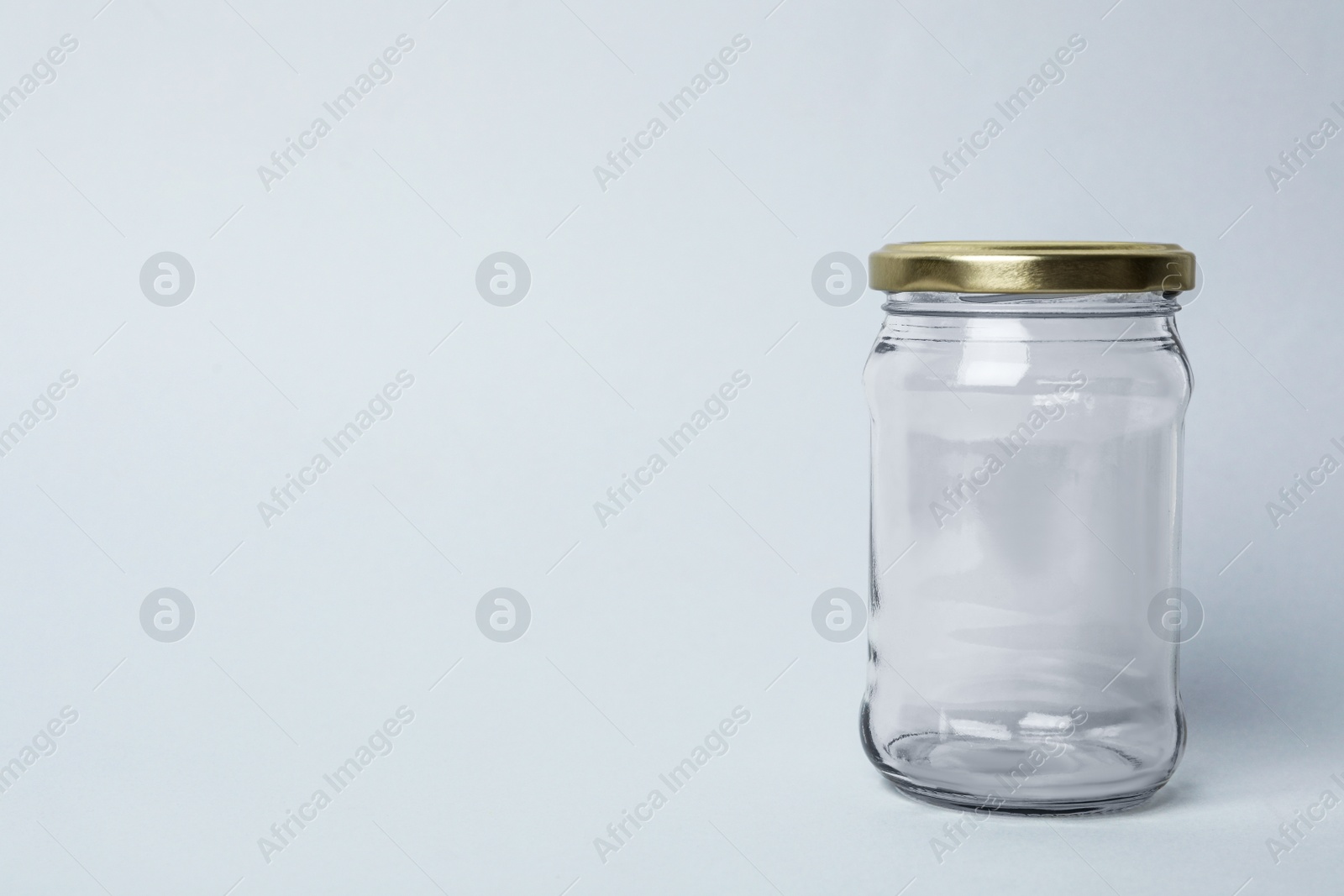 Photo of Closed empty glass jar on light background, space for text