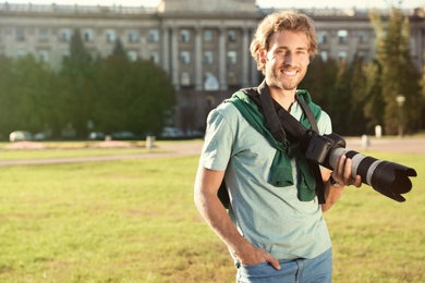 Photo of Handsome male photographer holding professional camera on street. Space for text