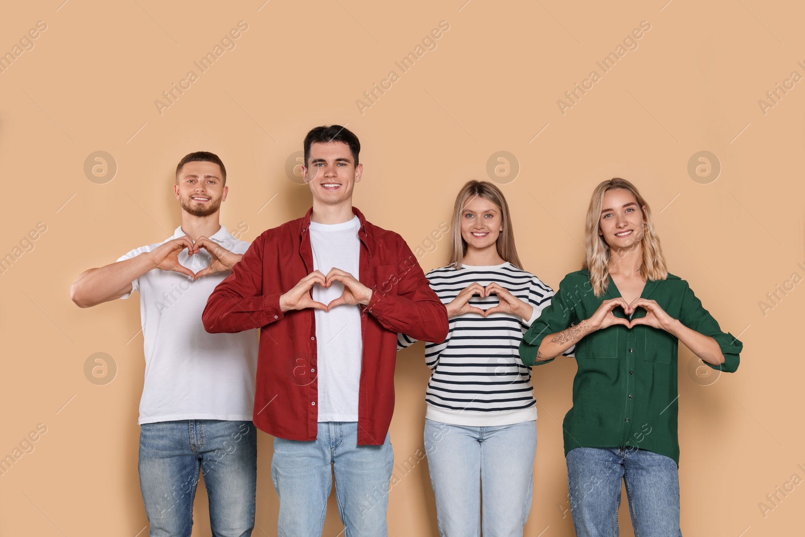 Photo of Happy volunteers making hearts with their hands on beige background