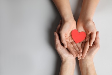 Young and elderly women holding red heart on light grey background, top view. Space for text