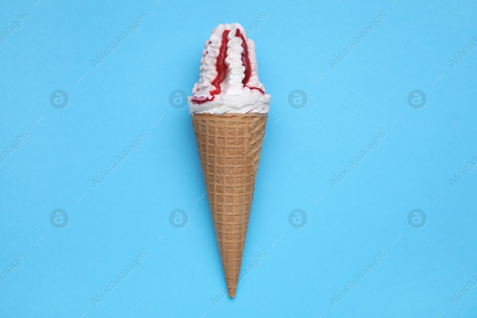 Photo of Delicious ice cream with raspberry jam in waffle cone on light blue background, top view