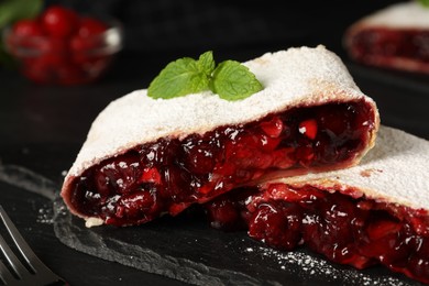 Photo of Delicious strudel with cherries, powdered sugar and mint on black table, closeup