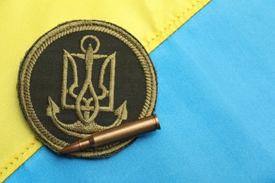 Bullet and military patch on Ukrainian flag, flat lay. Space for text