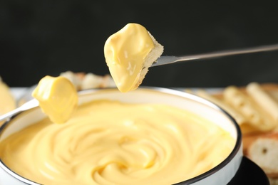 Photo of Pieces of bread over pot with delicious cheese fondue, closeup