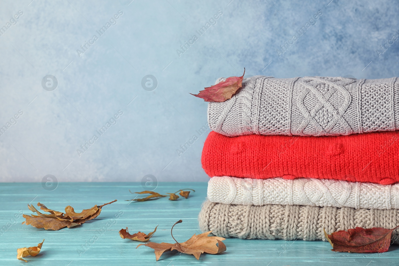 Photo of Stack of warm clothes with autumn leaves on table. Space for text