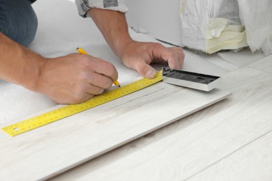 Photo of Professional worker using measuring tape and pen during installation of laminate flooring, closeup