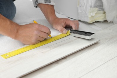 Professional worker using measuring tape and pen during installation of laminate flooring, closeup