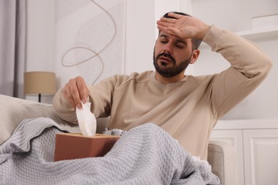 Photo of Sick man with tissues on sofa at home. Cold symptoms