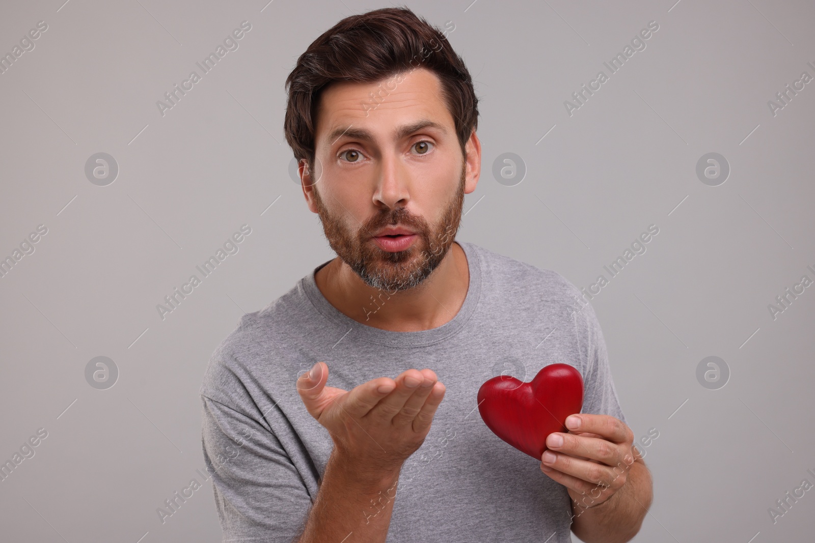Photo of Man holding red heart and blowing kiss on grey background
