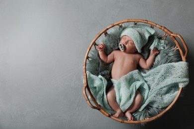 Photo of Cute newborn baby in wicker basket on grey background, top view. Space for text