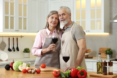 Happy senior couple with glasses of wine in kitchen