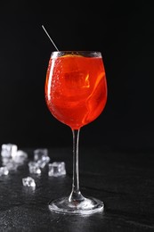 Glass of tasty Aperol spritz cocktail with orange slices and ice cubes on table against black background