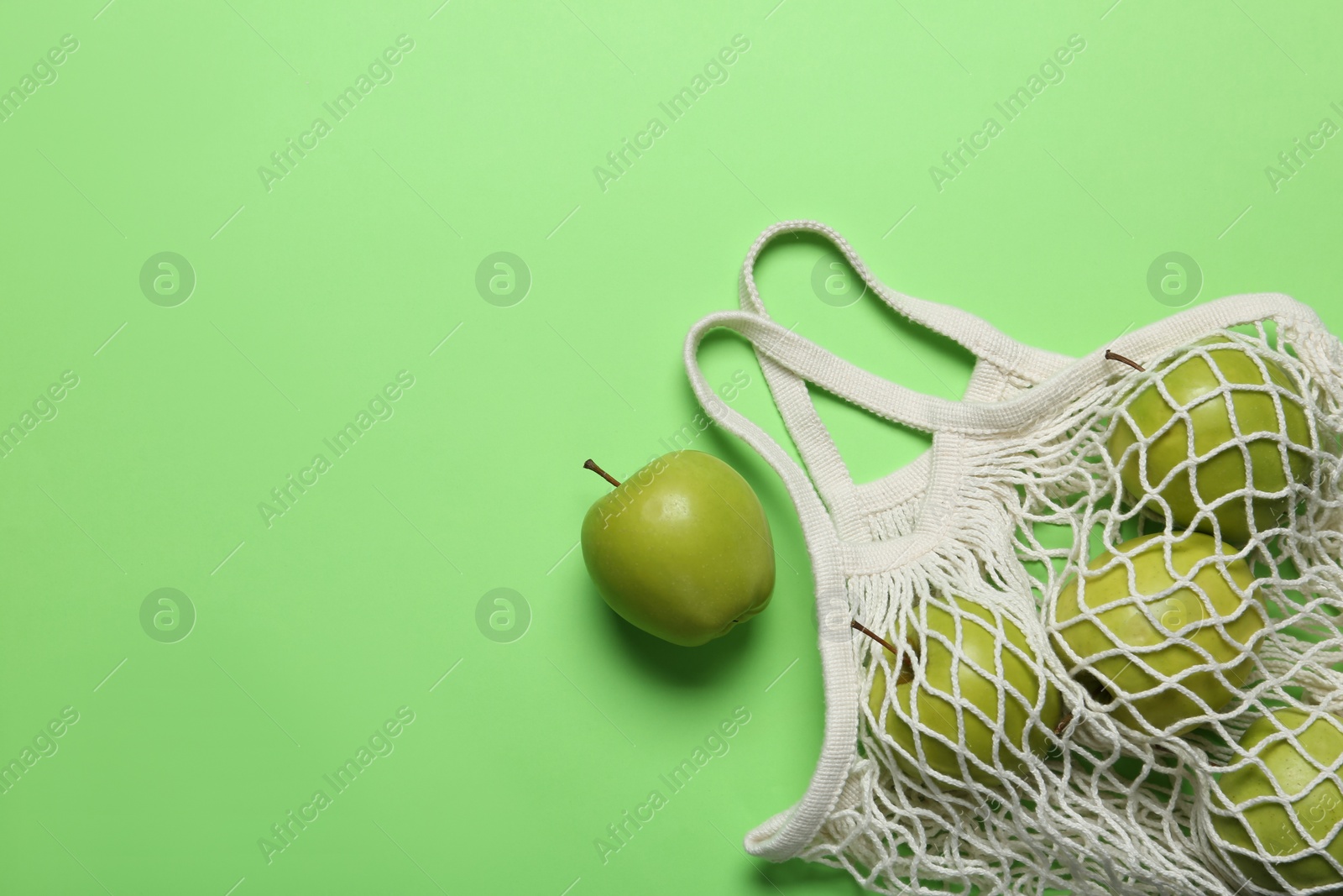 Photo of Net bag with juicy apples on green background, flat lay. Space for text